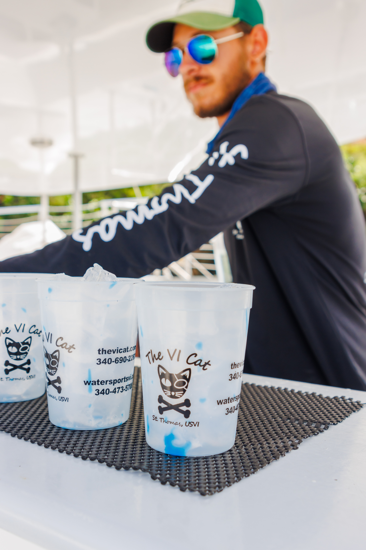 Man with sunglasses serving drinks in branded cups on a boat.