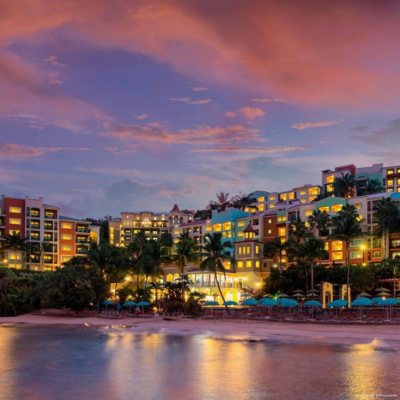 Colorful beachfront resort with palm trees at sunset.
