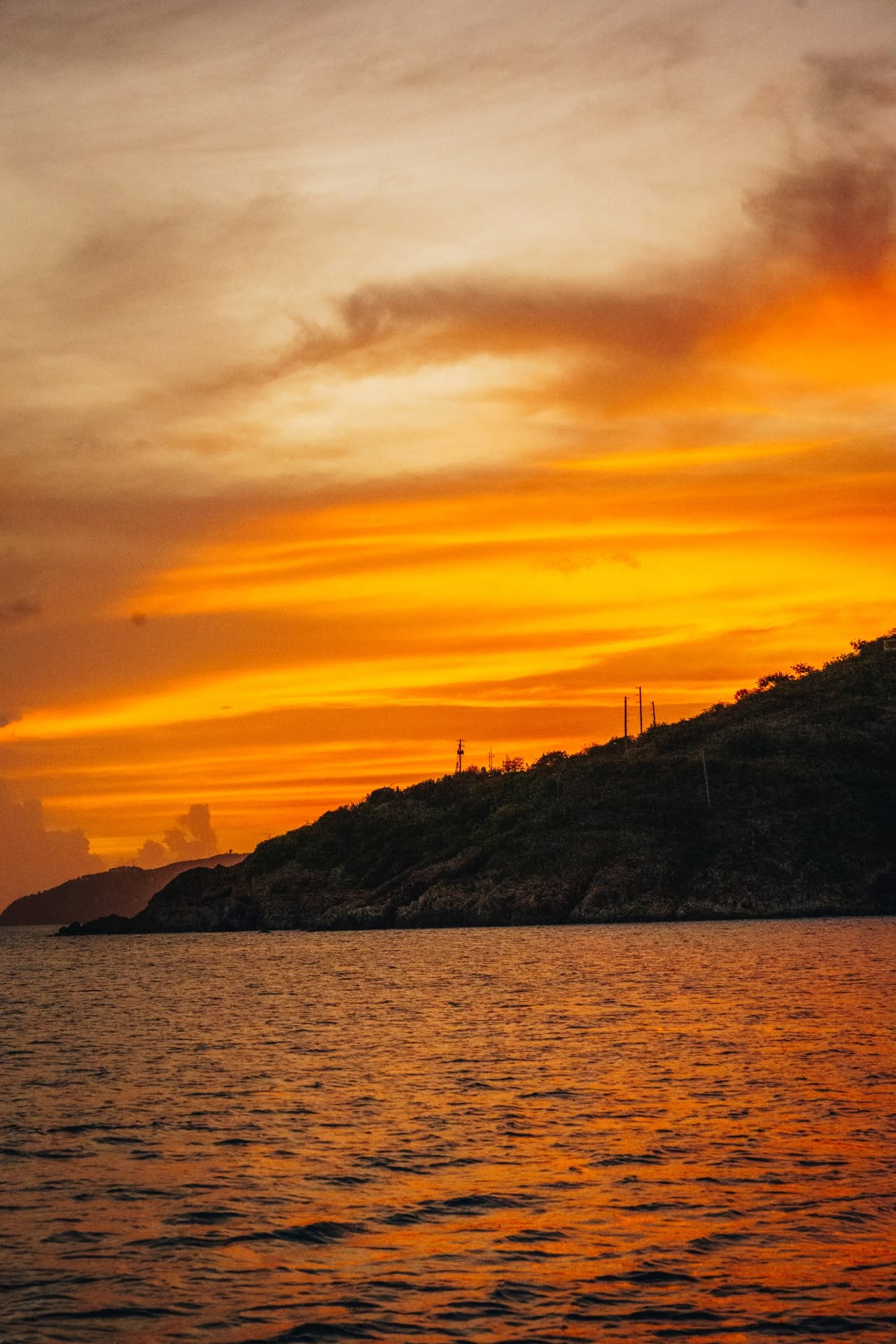 Sunset over a rocky coastline with vibrant orange and yellow clouds.