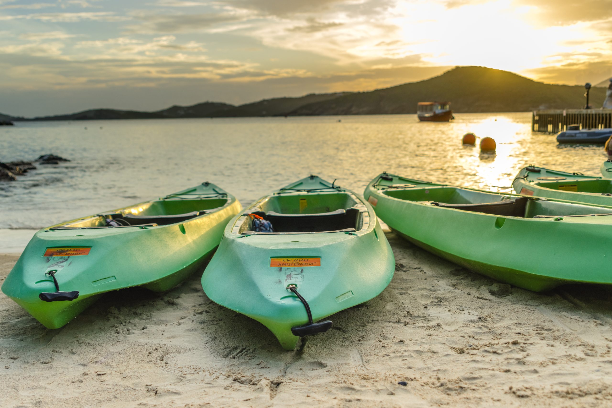Green kayaks on sandy beach near calm sea at sunset.