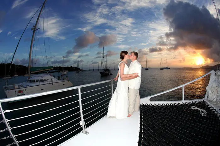 Couple kissing on yacht at sunset with sailboats in background.