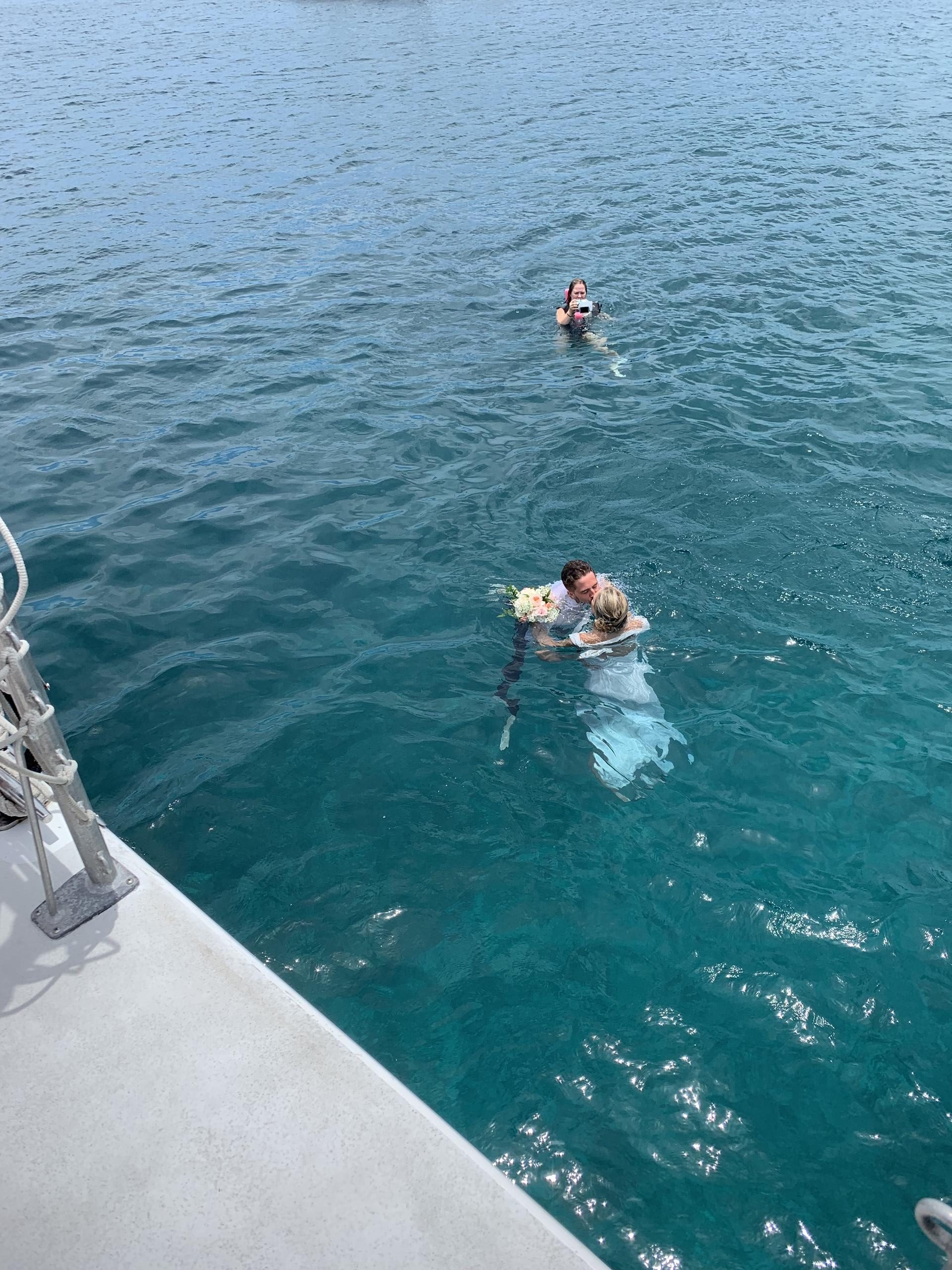People swimming near a boat in clear blue water.