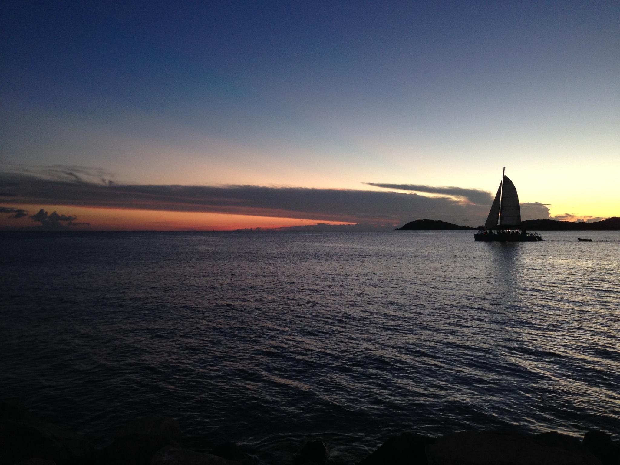 Sailboat on calm sea at sunset with distant islands.