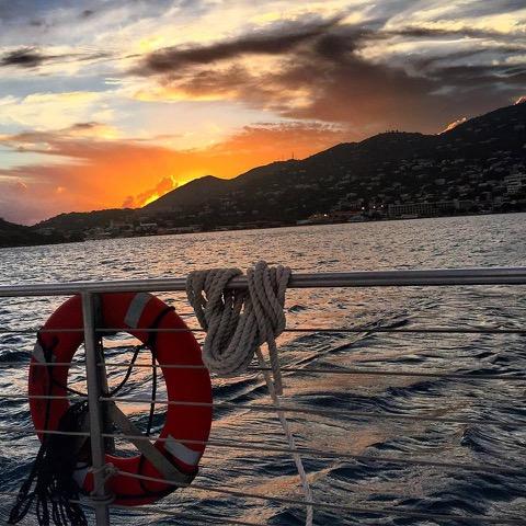 Sunset view from boat with lifebuoy; mountains and buildings in the distance.