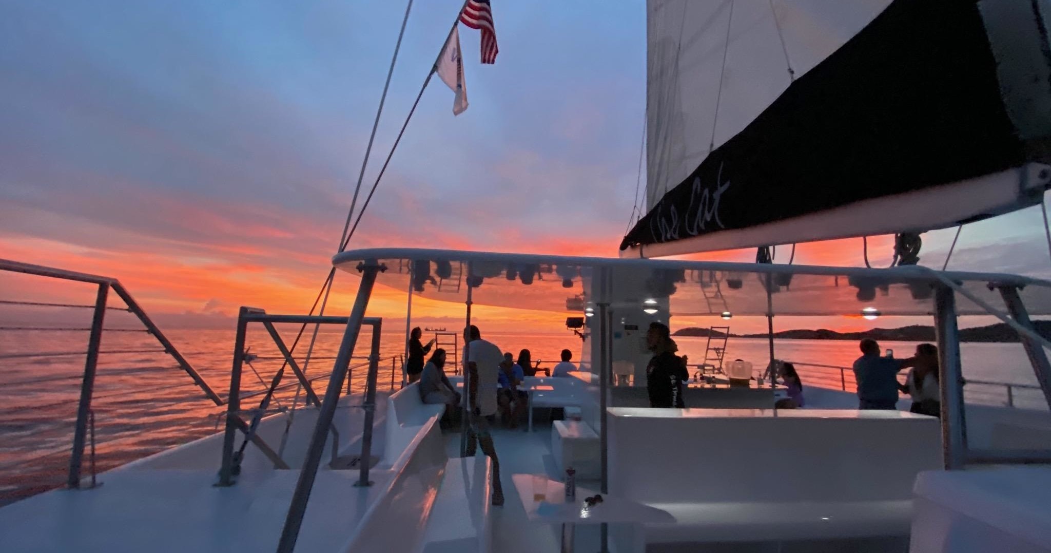 People on a boat at sunset with sails and flags.