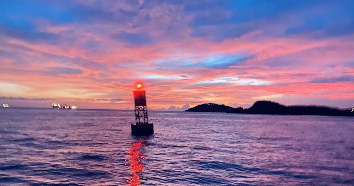 Vibrant sunset over ocean with a buoy and distant hills.