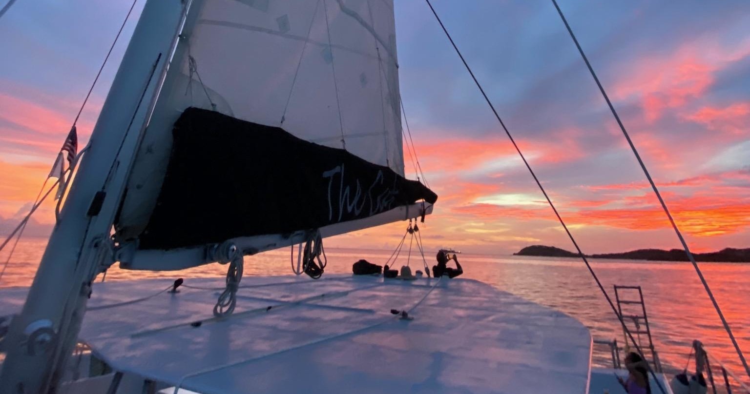 Silhouetted sailboat at sunset with vibrant pink and orange sky.