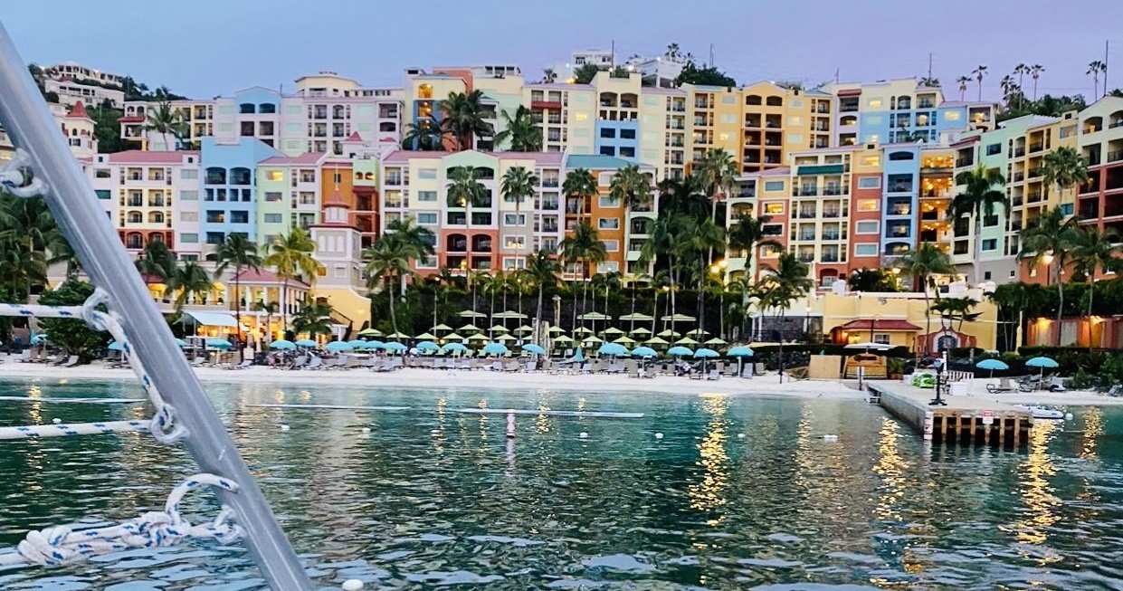 Colorful hillside buildings overlook a beach with umbrellas and a calm sea.