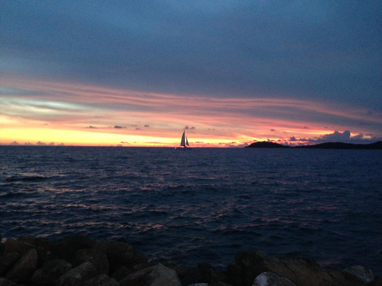 Sailboat on the ocean at sunset with colorful sky.