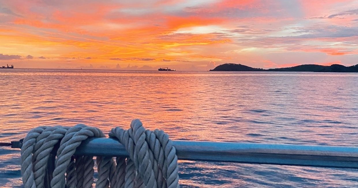Sunset over a calm ocean with rope on a railing.