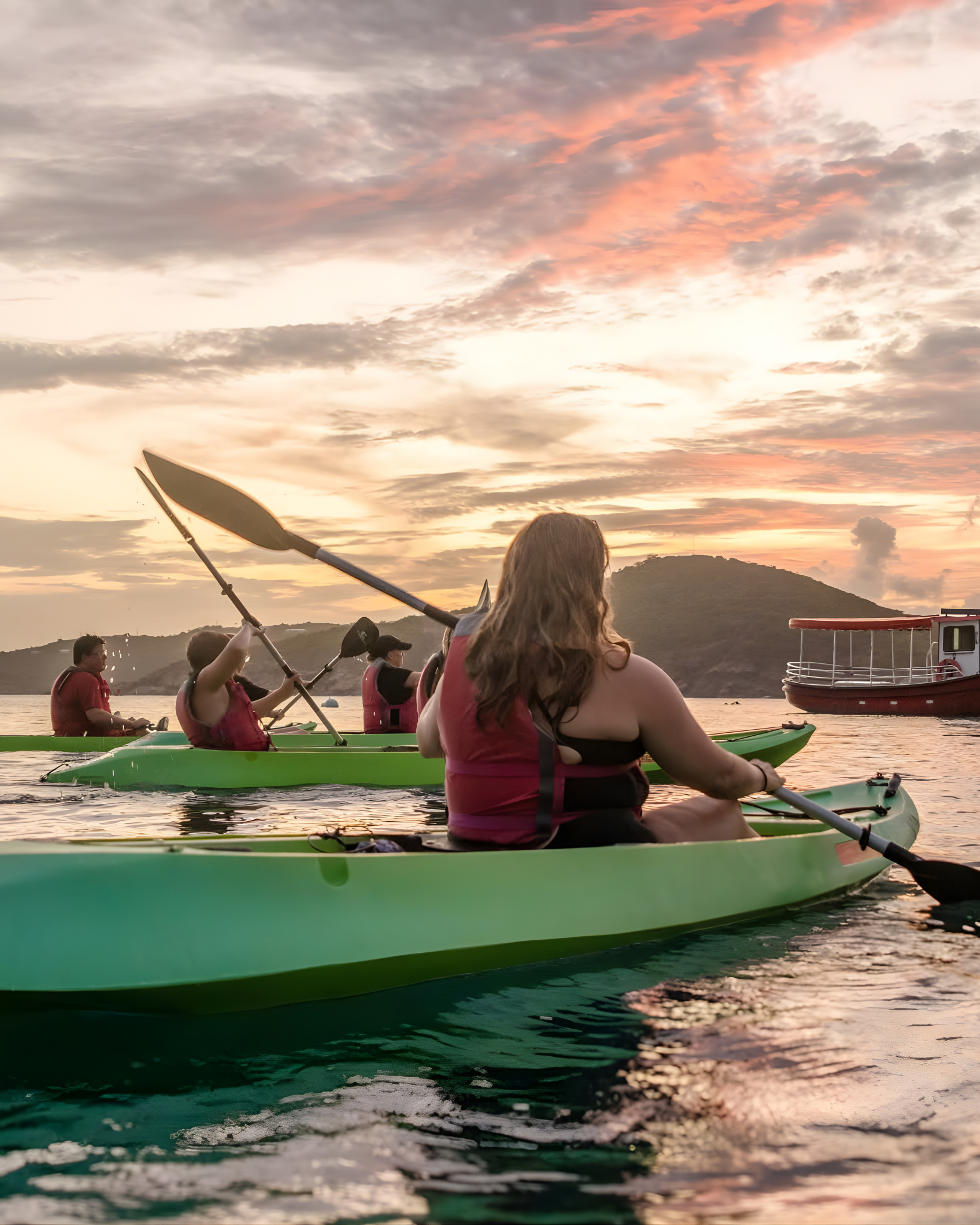 Group kayaking on a lake at sunset with mountains in the background.