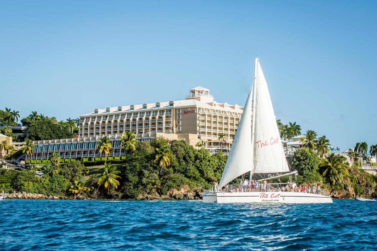Sailboat on water with a large hotel and palm trees in the background.