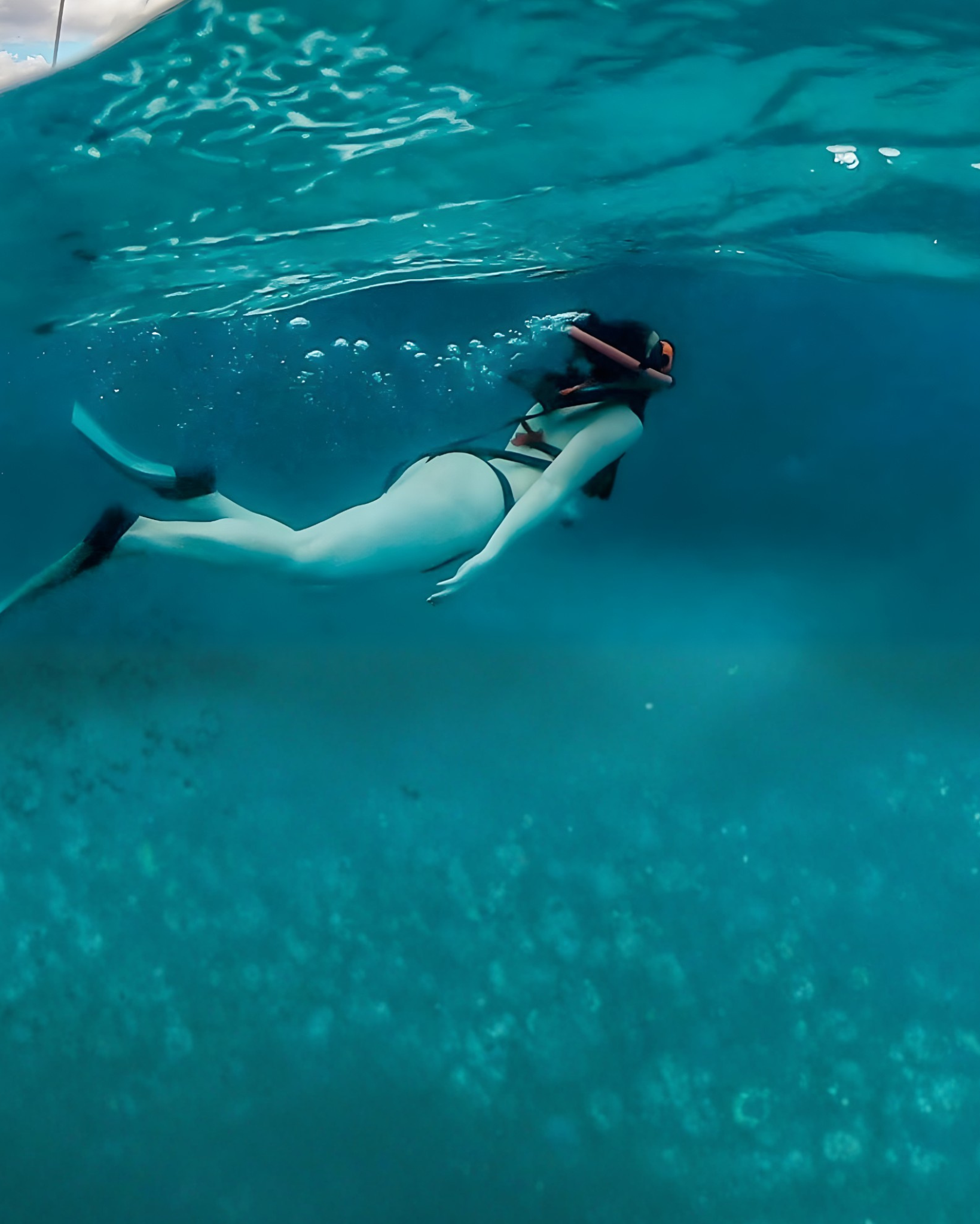 Person snorkeling underwater in clear blue water wearing fins and snorkel gear.