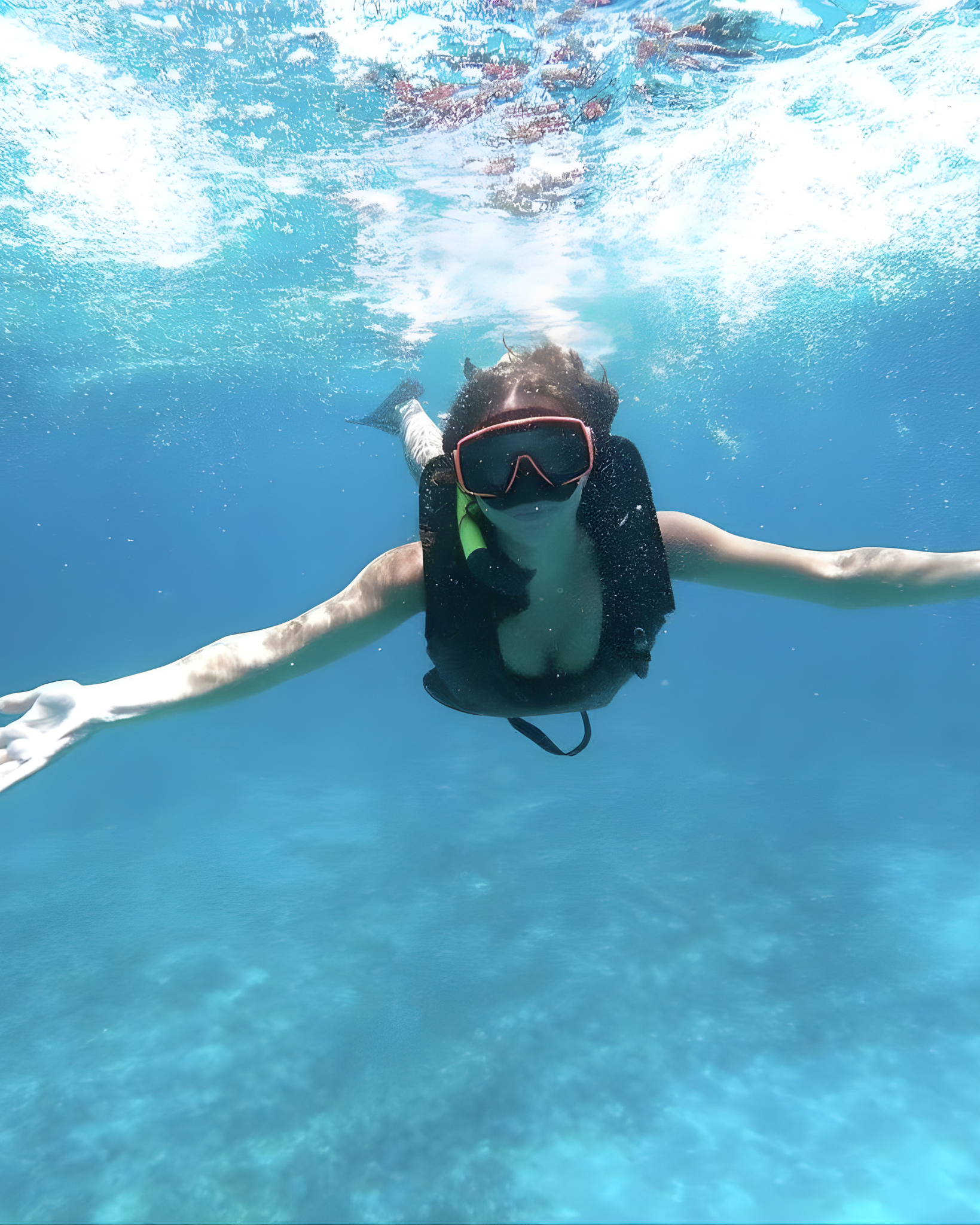 Person snorkeling underwater with arms outstretched and wearing goggles and snorkel.