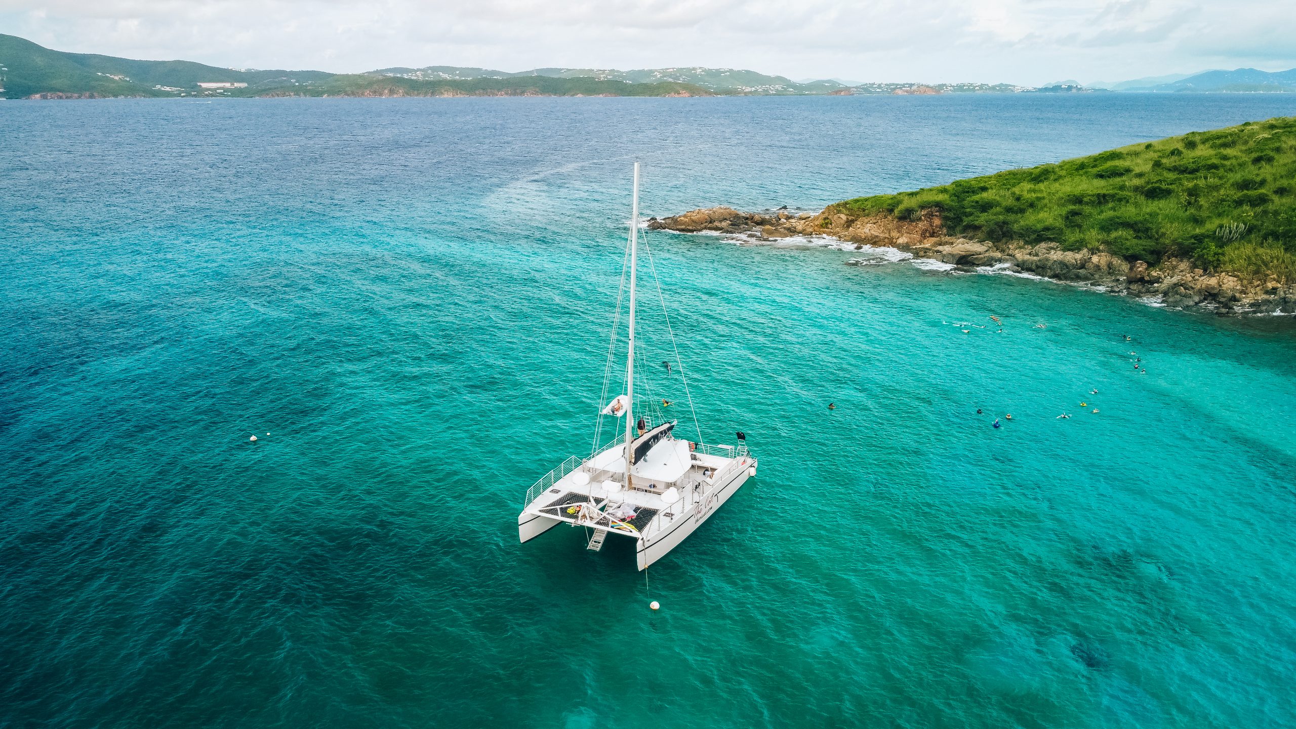 Catamaran sailing near a small island in clear turquoise water.